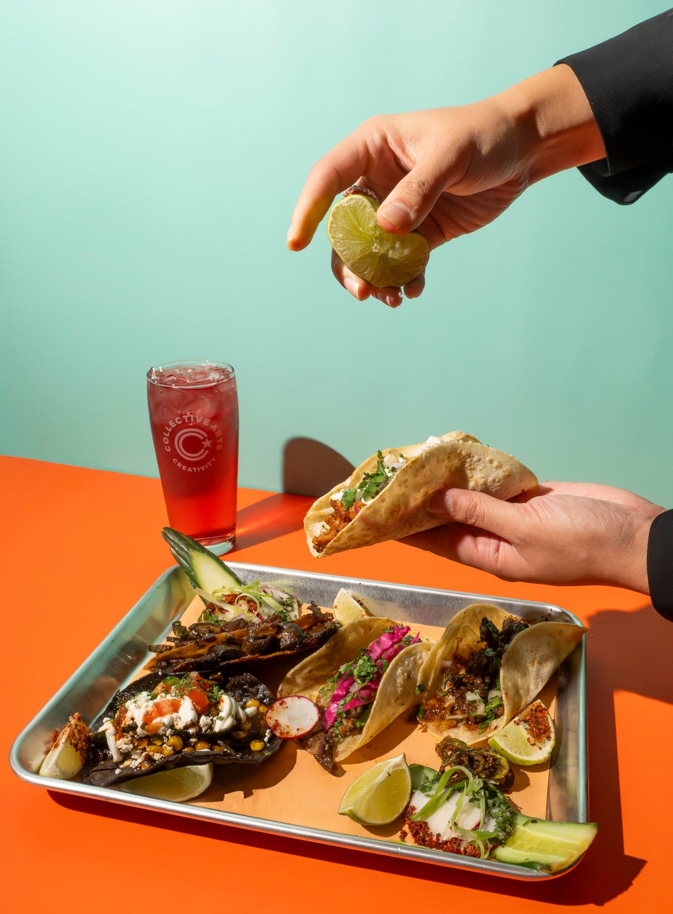 Person squeezing a fresh lime over a tray of authentic Mexican tacos with a cold beer in the background 